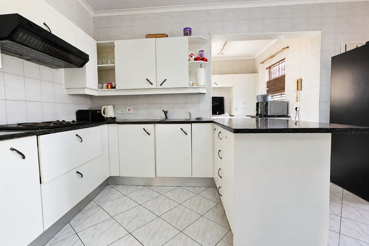 Functional kitchen featuring white cabinetry, granite countertops, a built-in hob with extractor fan, and tiled flooring, offering a clean and practical workspace.