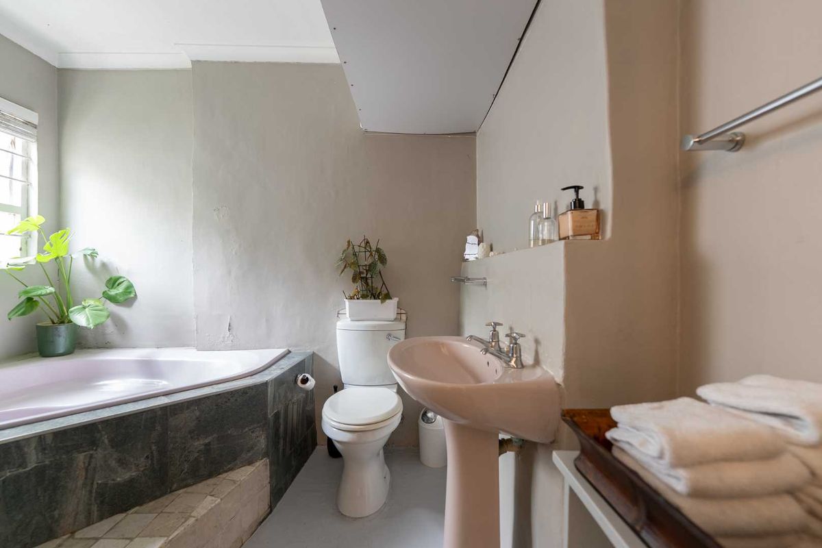 A dated bathroom featuring a corner bathtub with stone-look tiling, a pedestal sink, and a standard toilet, requiring cosmetic updates to the walls and ceiling.