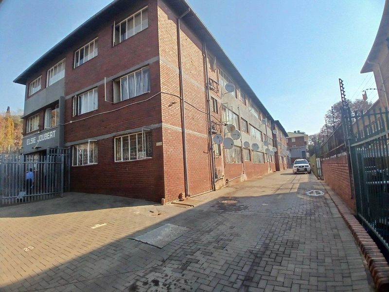Exterior view of a multi-story brick apartment building featuring a paved driveway, security gate, and perimeter electric fencing.
