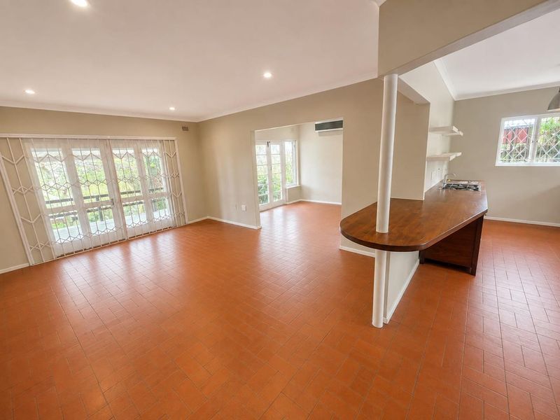 Spacious open-plan living and kitchen area featuring terracotta tile flooring, a built-in breakfast bar with cooktop, and direct access to the outdoor patio.