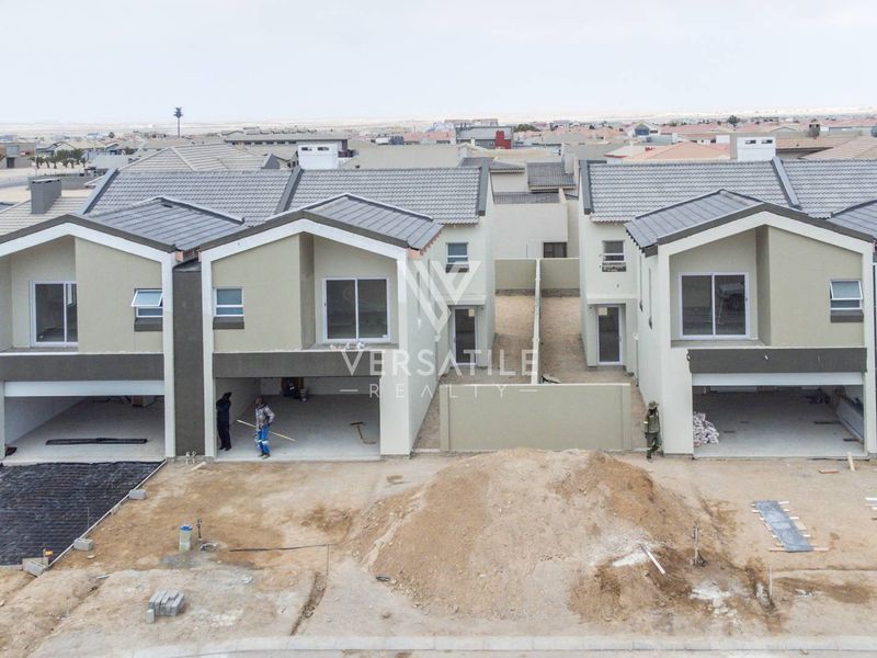 Aerial view of a townhouse development under construction, featuring modern facades, tiled roofs, and unfinished exterior grounds.