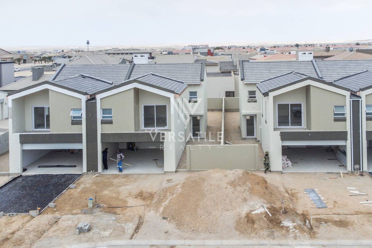 Aerial view of a townhouse development under construction, featuring modern facades, tiled roofs, and unfinished exterior grounds.