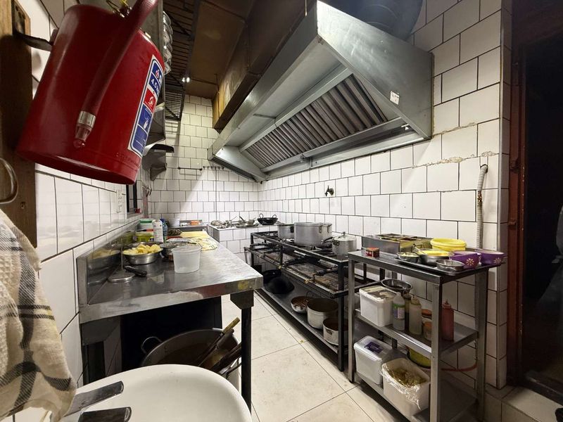 A functional commercial kitchen space featuring stainless steel work surfaces, a large extractor hood, gas cooking equipment, and tiled wall finishes.