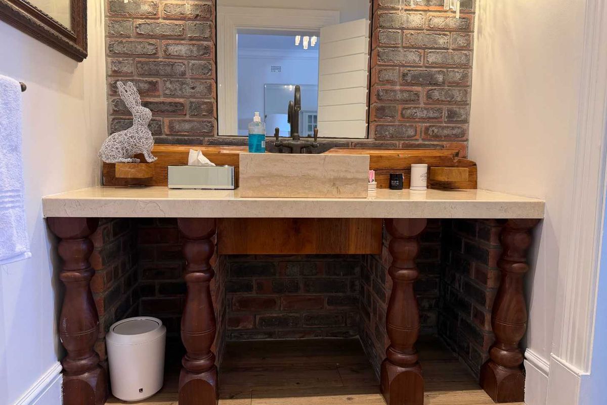 A rustic-style bathroom vanity featuring a stone basin, exposed brickwork, and decorative timber pillars, complemented by a large wall-mounted mirror.