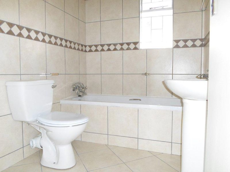 A functional bathroom featuring a pedestal basin, toilet, and built-in bathtub with neutral wall and floor tiling.