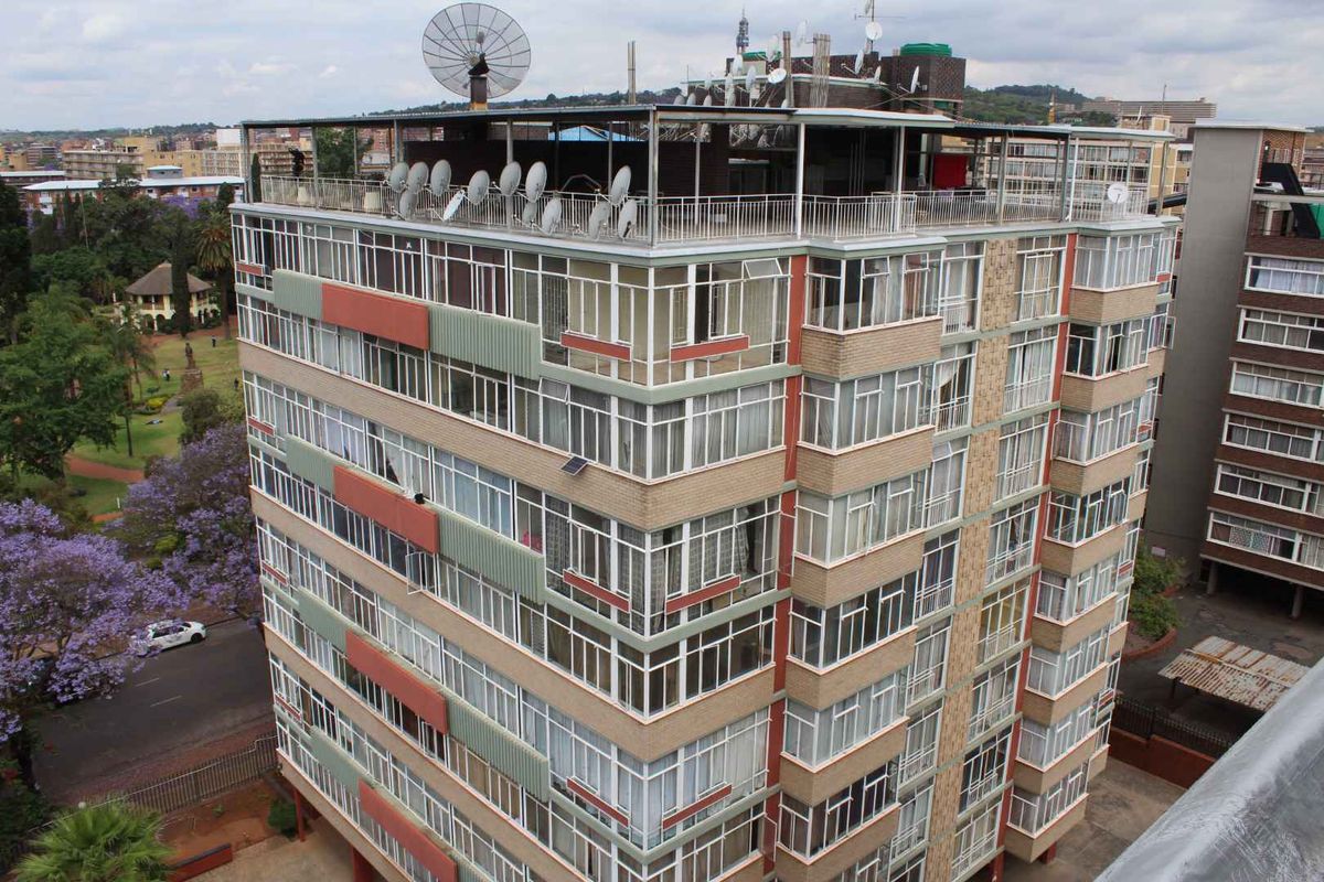 Aerial view of a multi-story apartment building featuring brick exterior, extensive window glazing, and a rooftop area with multiple satellite dishes.