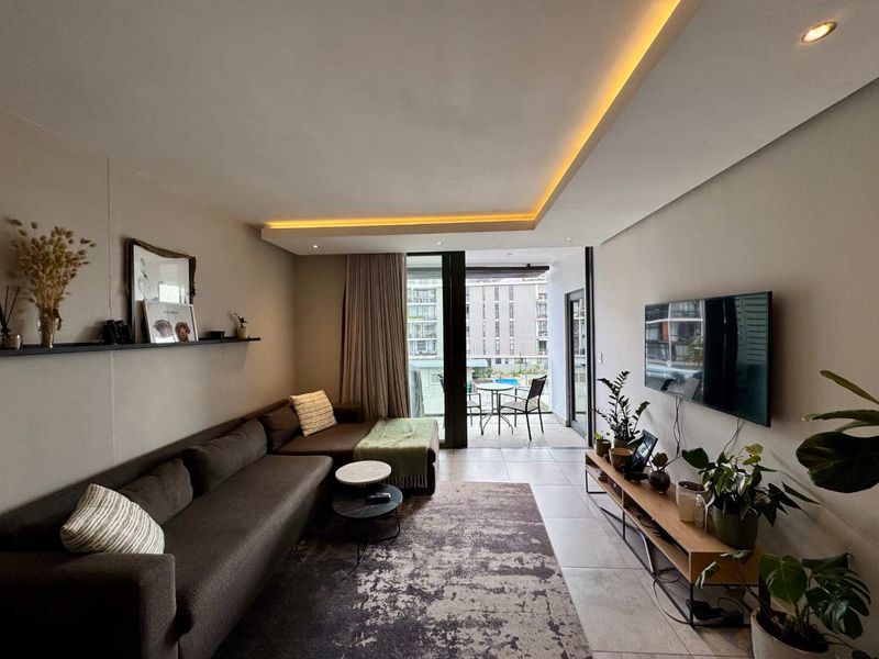 Modern living room featuring recessed cove lighting, tiled flooring, and large sliding glass doors providing seamless access to the balcony.