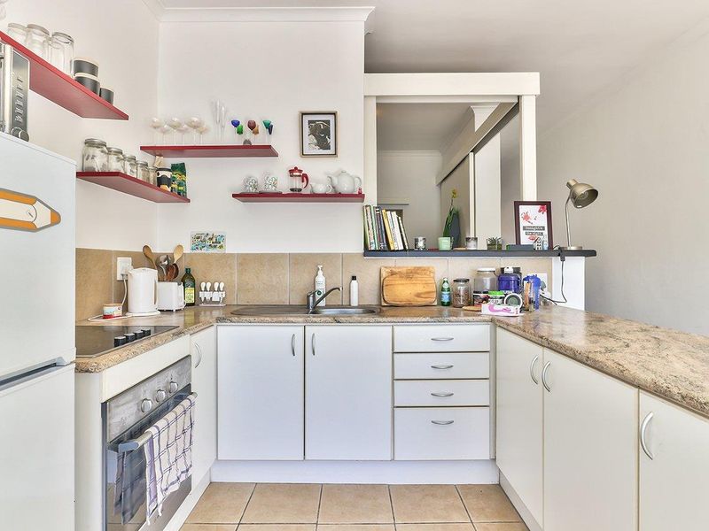 Compact kitchen featuring white cabinetry, laminate countertops, tiled backsplash, built-in oven, and electric hob with open shelving for storage.