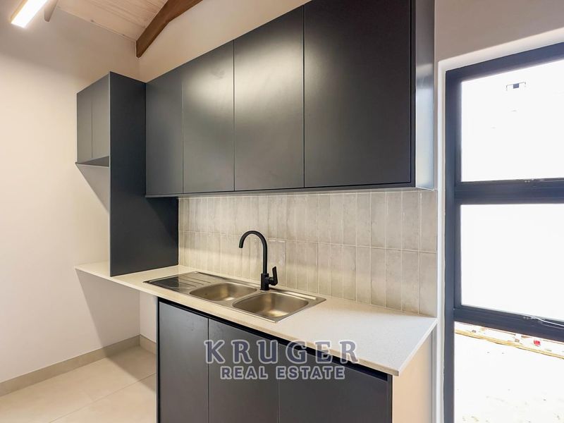 Modern kitchen featuring sleek dark cabinetry, stone countertops, a stainless steel double sink with matte black tapware, and exposed timber rafters.