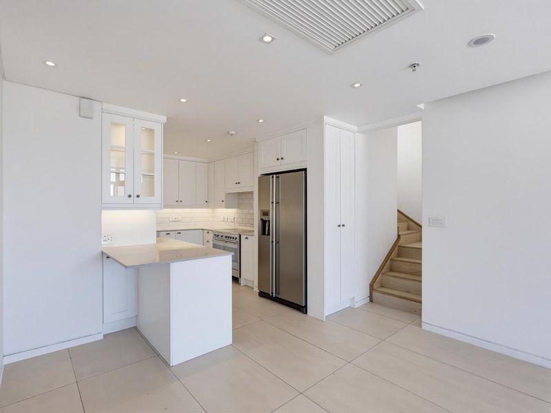 Modern kitchen featuring white cabinetry, stone countertops, subway tile backsplash, and integrated appliances, adjacent to a staircase in an open-plan layout.