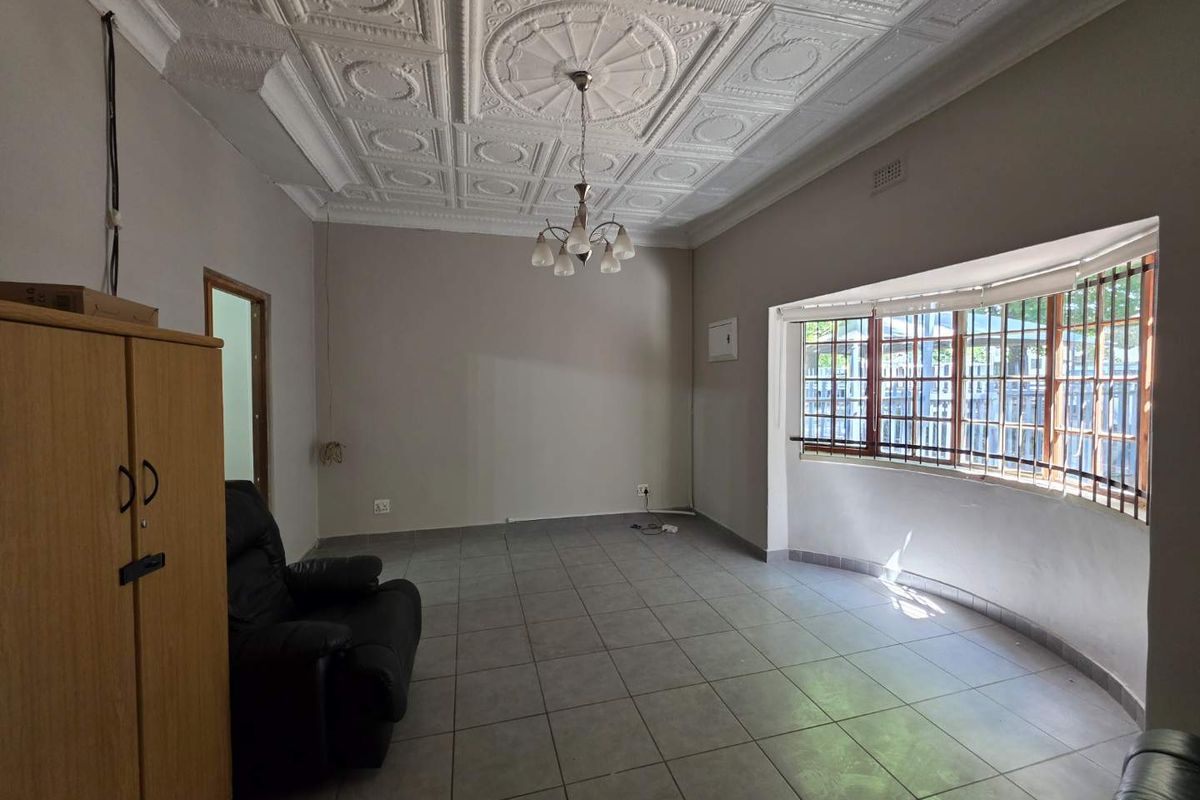 Spacious living room featuring a decorative pressed metal ceiling, large bay window, and neutral tiled flooring.