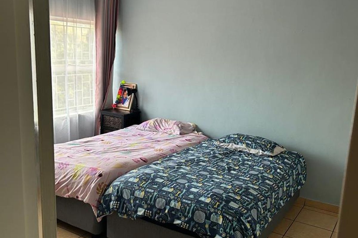 A standard bedroom featuring tiled flooring, a ceiling fan, and a window with security bars.