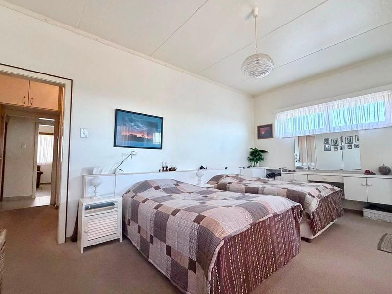 Spacious bedroom featuring built-in vanity and headboard cabinetry, neutral carpet flooring, and classic ceiling tiles, offering a functional layout with potential for modernization.