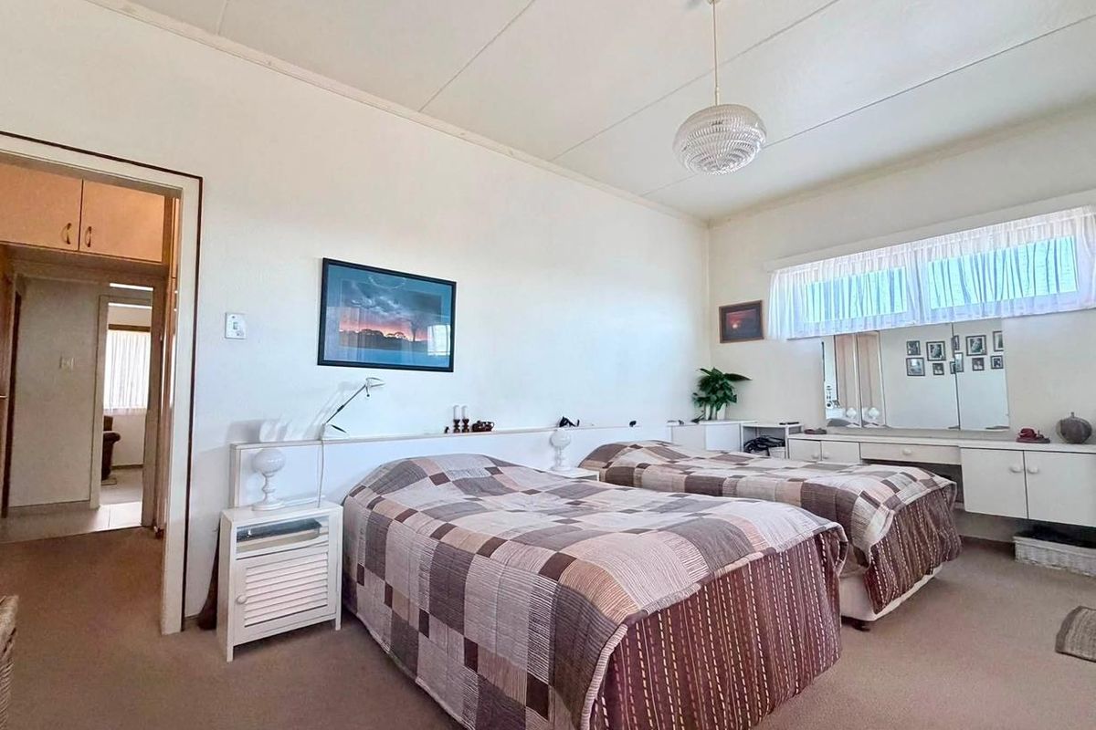 Spacious bedroom featuring built-in vanity and headboard cabinetry, neutral carpet flooring, and classic ceiling tiles, offering a functional layout with potential for modernization.
