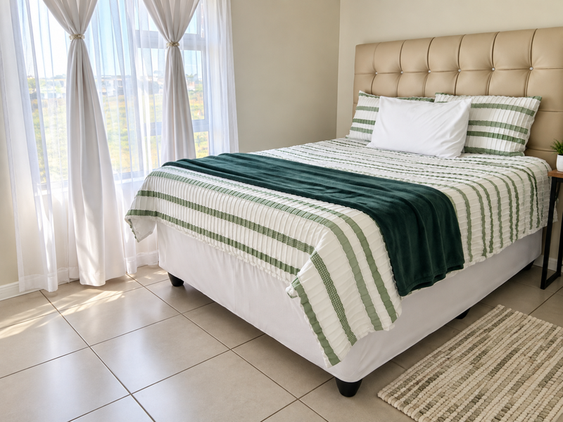 A bright and well-maintained bedroom featuring neutral tiled flooring and a large window that allows for ample natural light.