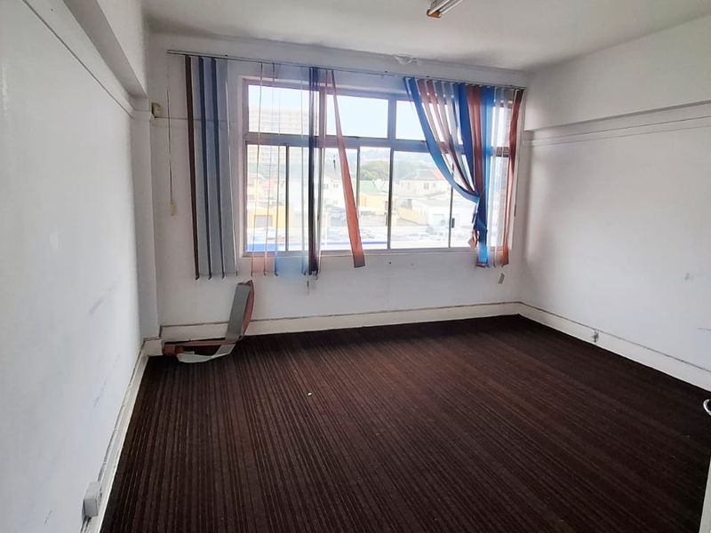 An empty office space featuring large windows, dark carpet flooring, and neutral walls, suitable for a professional workspace or meeting room.