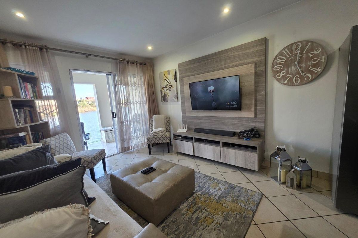 A well-maintained living room featuring a built-in media unit, tiled flooring, and a sliding glass door providing access to an outdoor area.