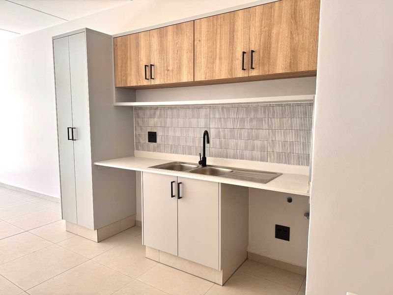 A modern, clean kitchen area featuring light grey and wood-look cabinetry, a stainless steel sink with a black tap, and a stylish tiled backsplash.