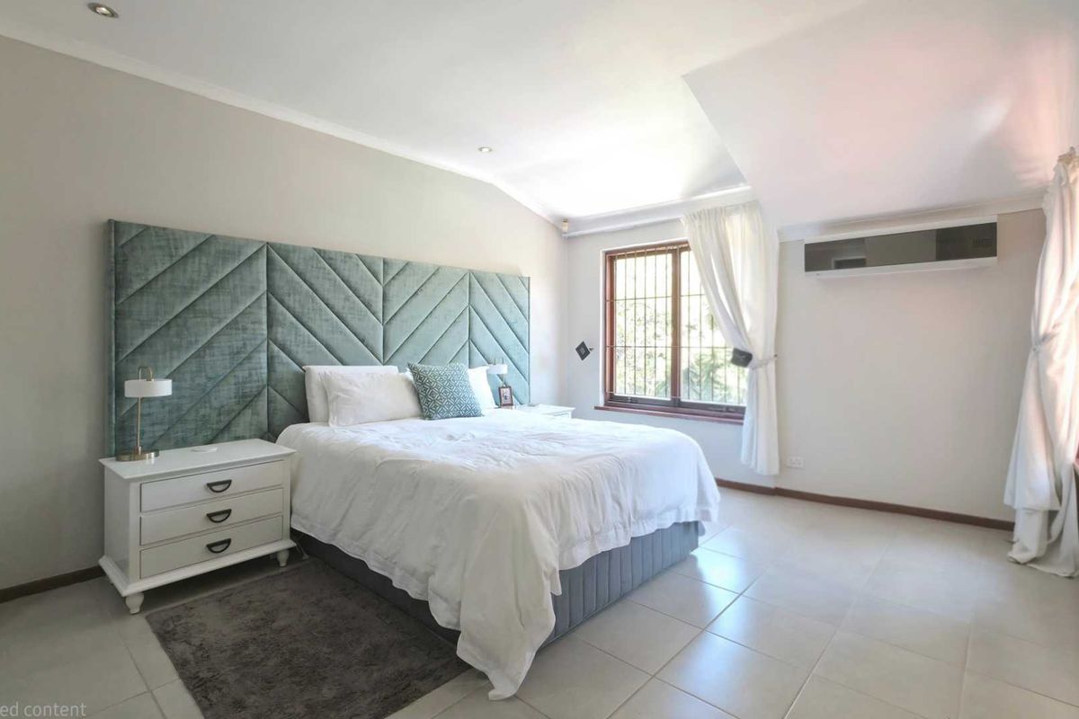 A spacious bedroom featuring tiled flooring, a built-in headboard, recessed ceiling lighting, and a wall-mounted air conditioning unit.