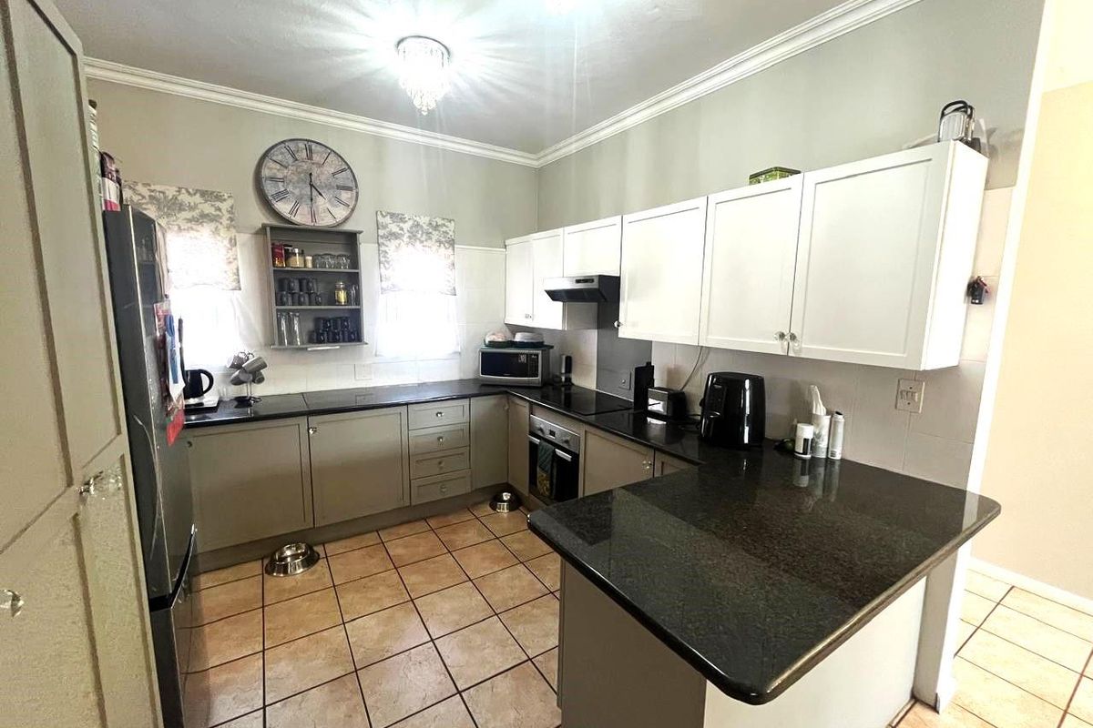A functional kitchen featuring dark granite countertops, white upper cabinetry, grey lower cabinetry, tiled flooring, and a built-in oven with an extractor fan.