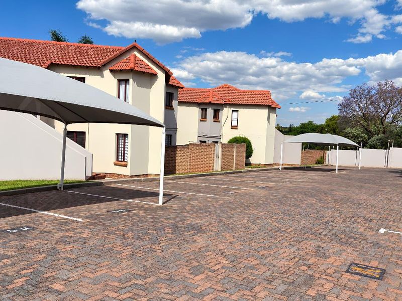 Exterior view of the apartment complex featuring a paved parking area with covered carports and well-maintained building facades.