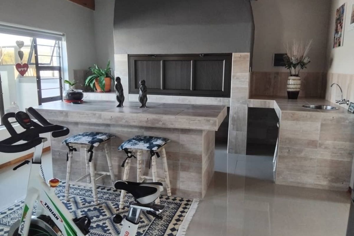 Indoor entertainment area featuring a built-in braai, tiled breakfast bar, and a small prep sink with tiled splashbacks and exposed timber ceiling beams.