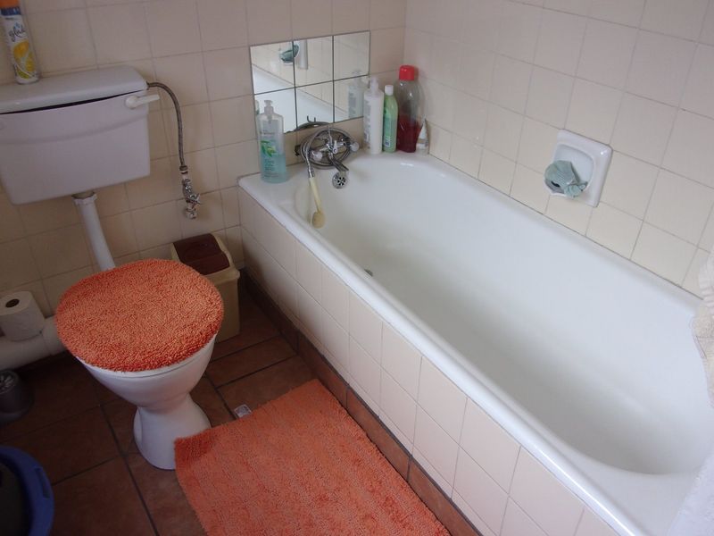A functional bathroom featuring a standard bathtub, toilet, and dated ceramic wall and floor tiling, offering potential for a modern renovation.