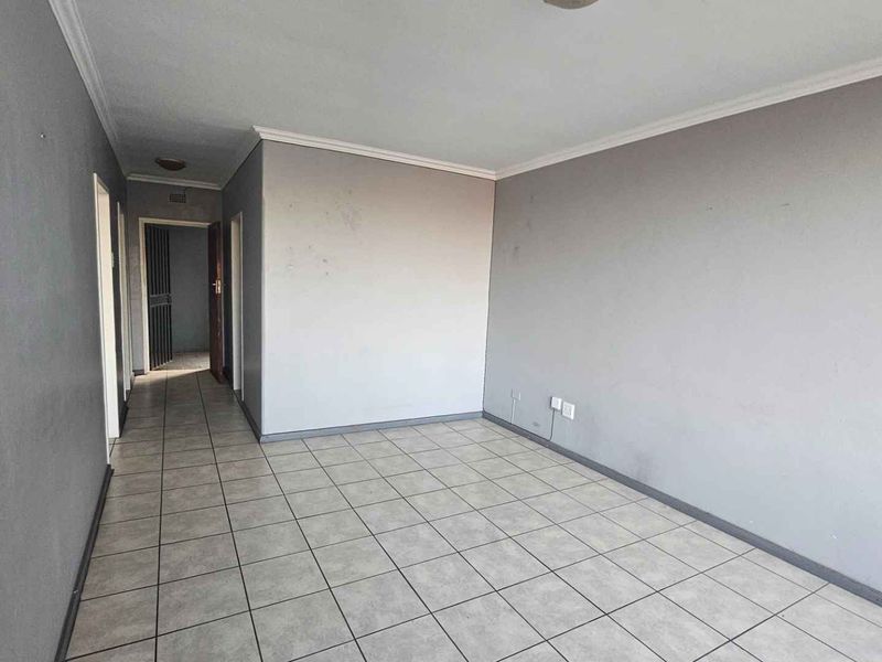 An empty living room featuring neutral grey walls and ceramic floor tiles, providing a blank canvas for potential interior design updates.