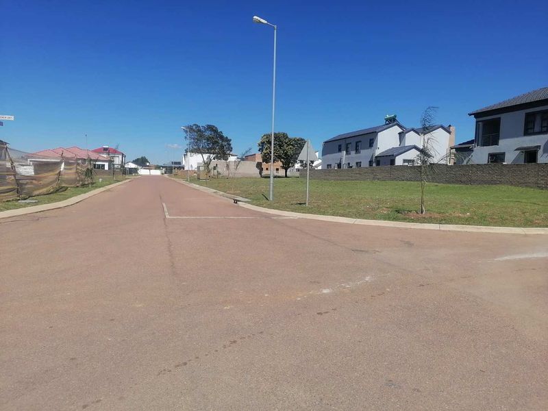 A clear street view of a residential development area featuring paved roads, concrete curbing, and established boundary walls in a suburban setting.