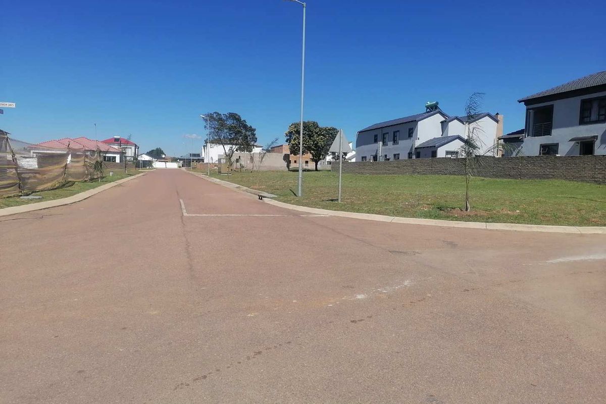 A clear street view of a residential development area featuring paved roads, concrete curbing, and established boundary walls in a suburban setting.