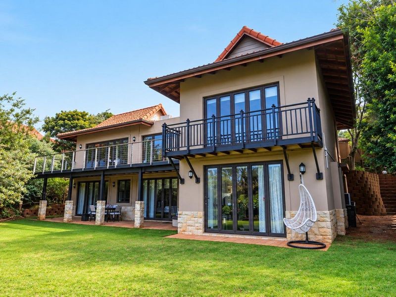 Rear view of a two-story house featuring a covered patio, upper-level balcony, stone cladding accents, and folding glass doors opening onto a landscaped garden.