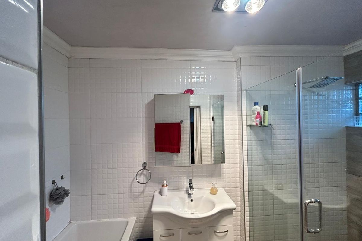 A functional bathroom featuring a vanity basin, a bathtub, and a separate glass-enclosed shower with white wall tiling.