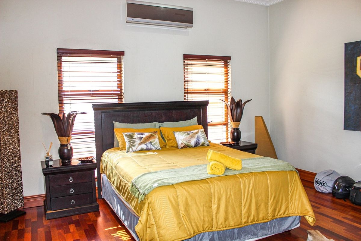 A well-maintained bedroom featuring polished hardwood flooring, dual windows with fitted wooden blinds, and a wall-mounted air conditioning unit.