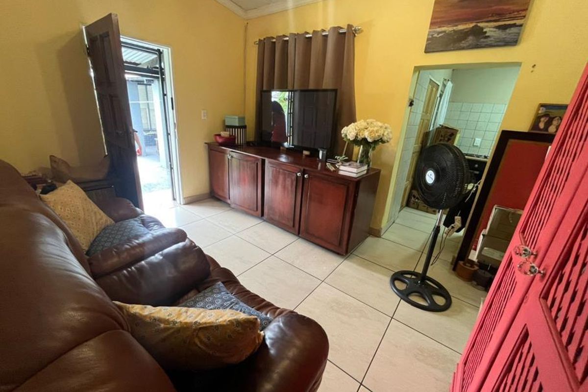A living room featuring tiled flooring and direct access to an outdoor area, with an adjacent view into the kitchen space.