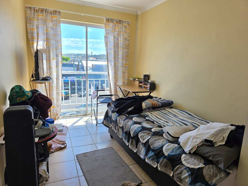 A bedroom featuring tiled flooring and a sliding glass door that opens onto a balcony with an urban view.