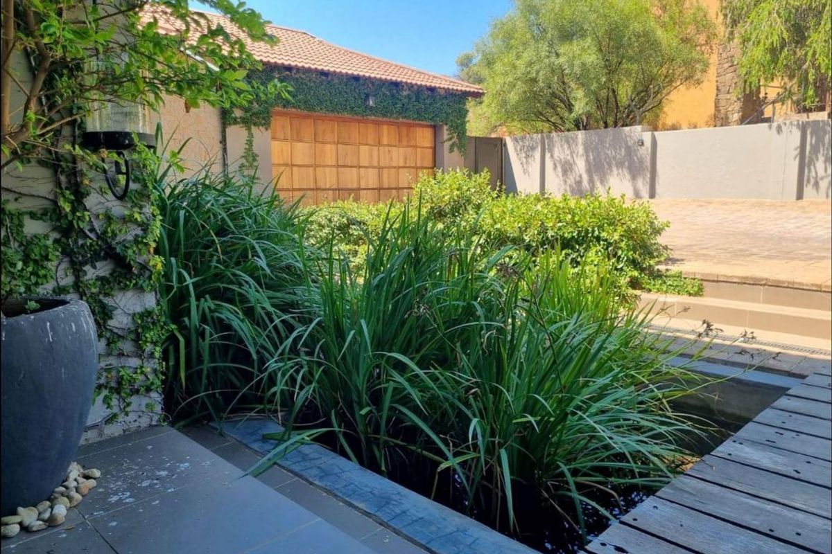 A well-maintained outdoor area featuring a water feature, timber decking, and a view towards a garage with a wooden door and climbing greenery.