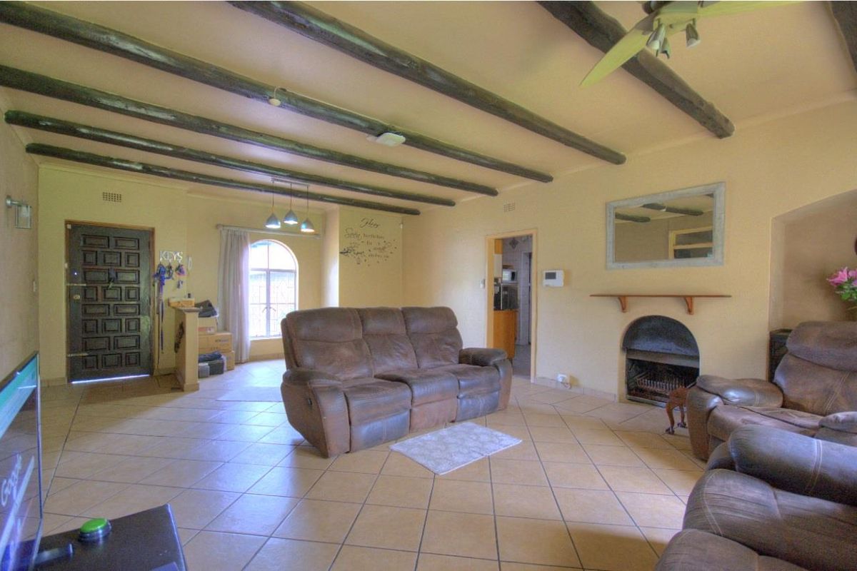 Spacious living room featuring exposed timber ceiling beams, tiled flooring, and a built-in fireplace, offering a warm and traditional atmosphere.