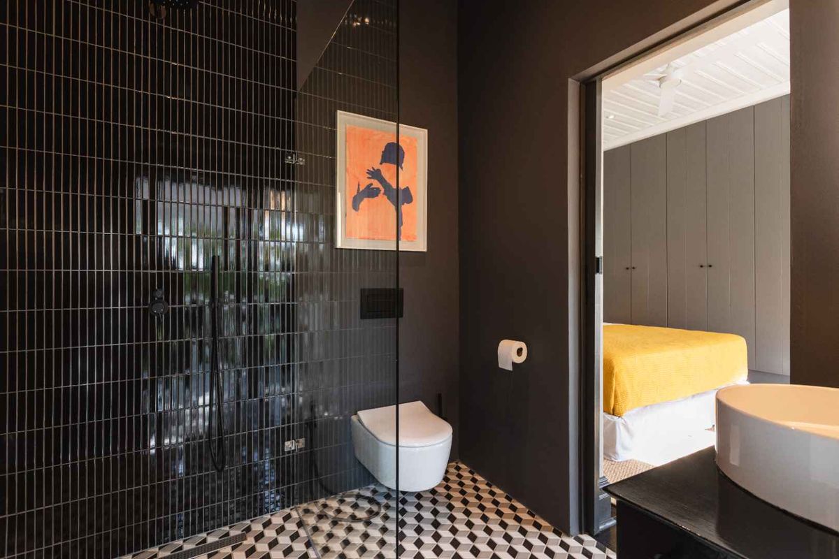 Modern bathroom featuring a walk-in shower with dark vertical tiling, a wall-hung toilet, and a stylish vessel sink, adjacent to a bedroom.