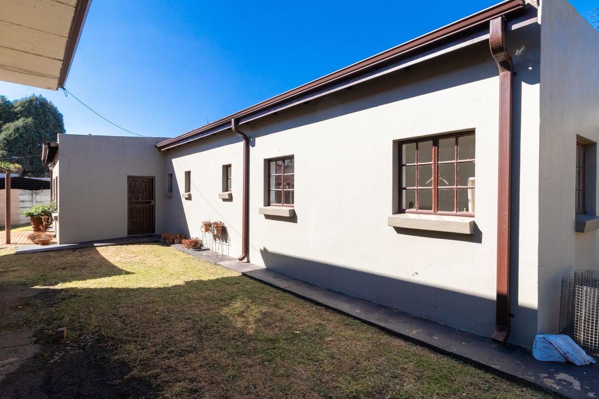 A view of the rear exterior of the house, featuring a paved walkway, lawn area, and security-fitted windows and doors.
