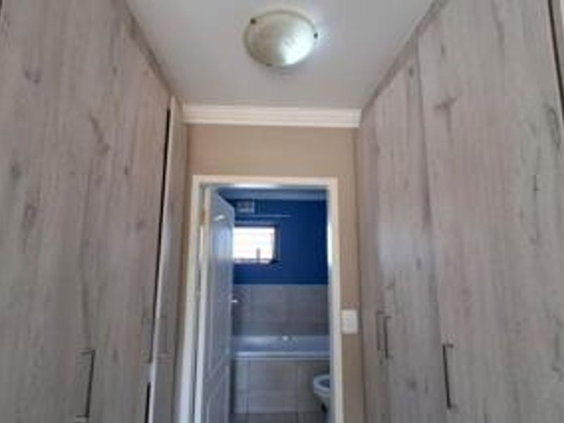 A hallway featuring extensive built-in cupboards with wood-look finish, leading directly into a bathroom.