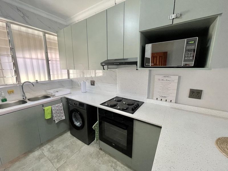 Modern kitchen featuring sage green cabinetry, white quartz countertops, integrated appliances including an oven and hob, and tiled flooring.