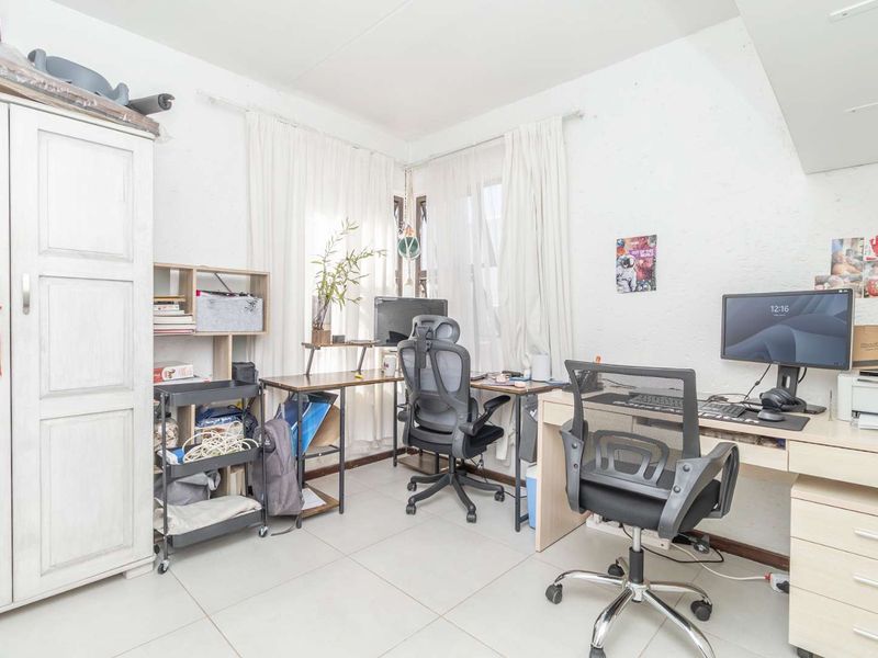 A functional home office space featuring tiled flooring and corner windows, providing natural light and a practical layout for a workspace.
