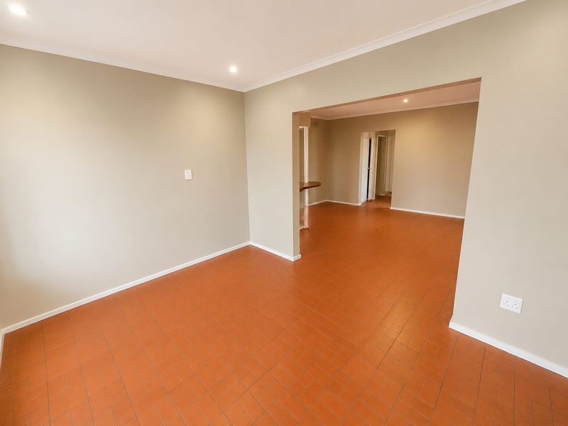 An empty, open-plan living area featuring terracotta tile flooring, recessed downlighting, and a neutral color palette, providing a versatile space for customization.