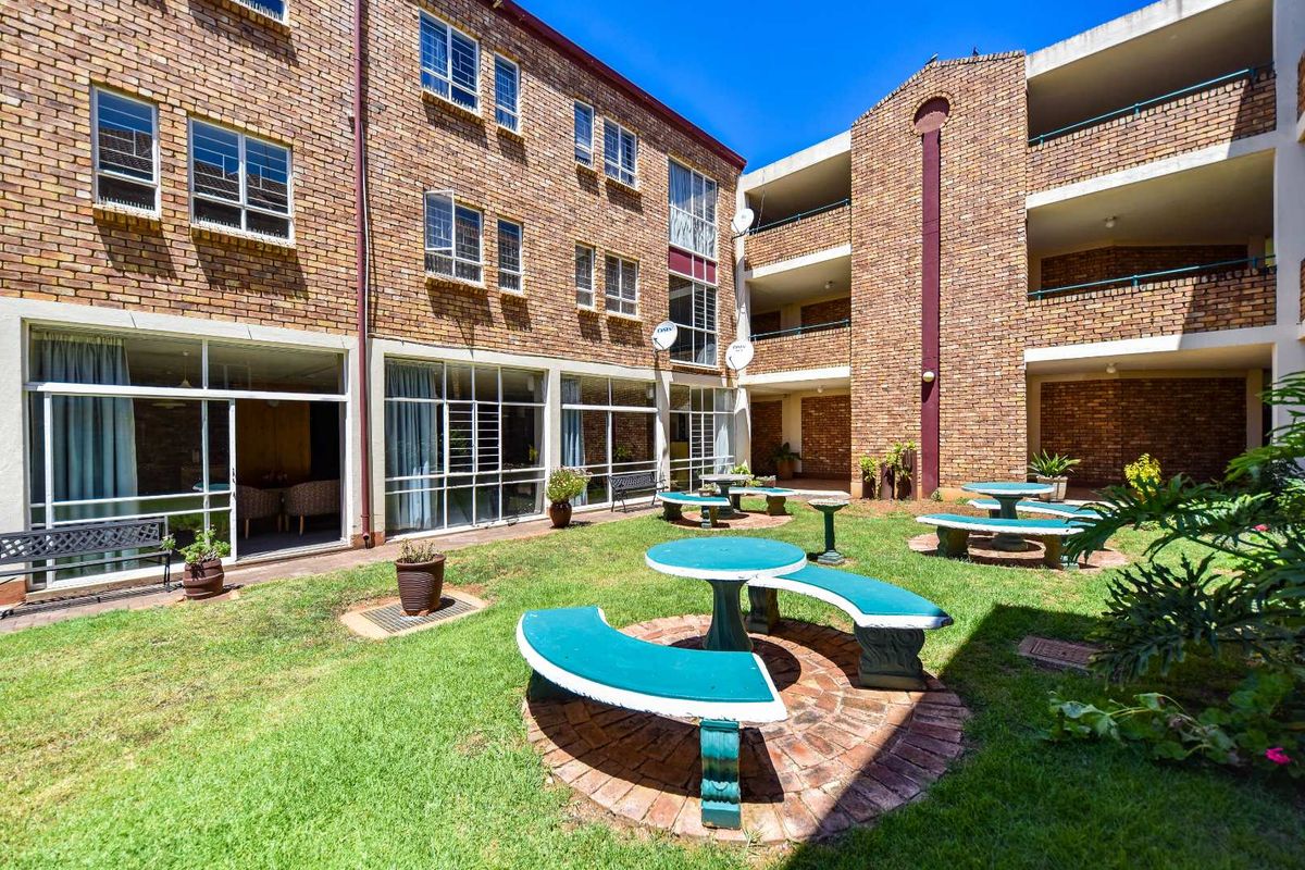 A well-maintained communal garden courtyard featuring brick building facades, multi-level balconies, and fixed concrete seating areas within a retirement village setting.
