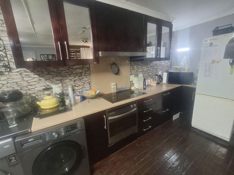 A functional kitchen featuring dark wood cabinetry, a built-in oven with an electric hob, and a stone-look backsplash.