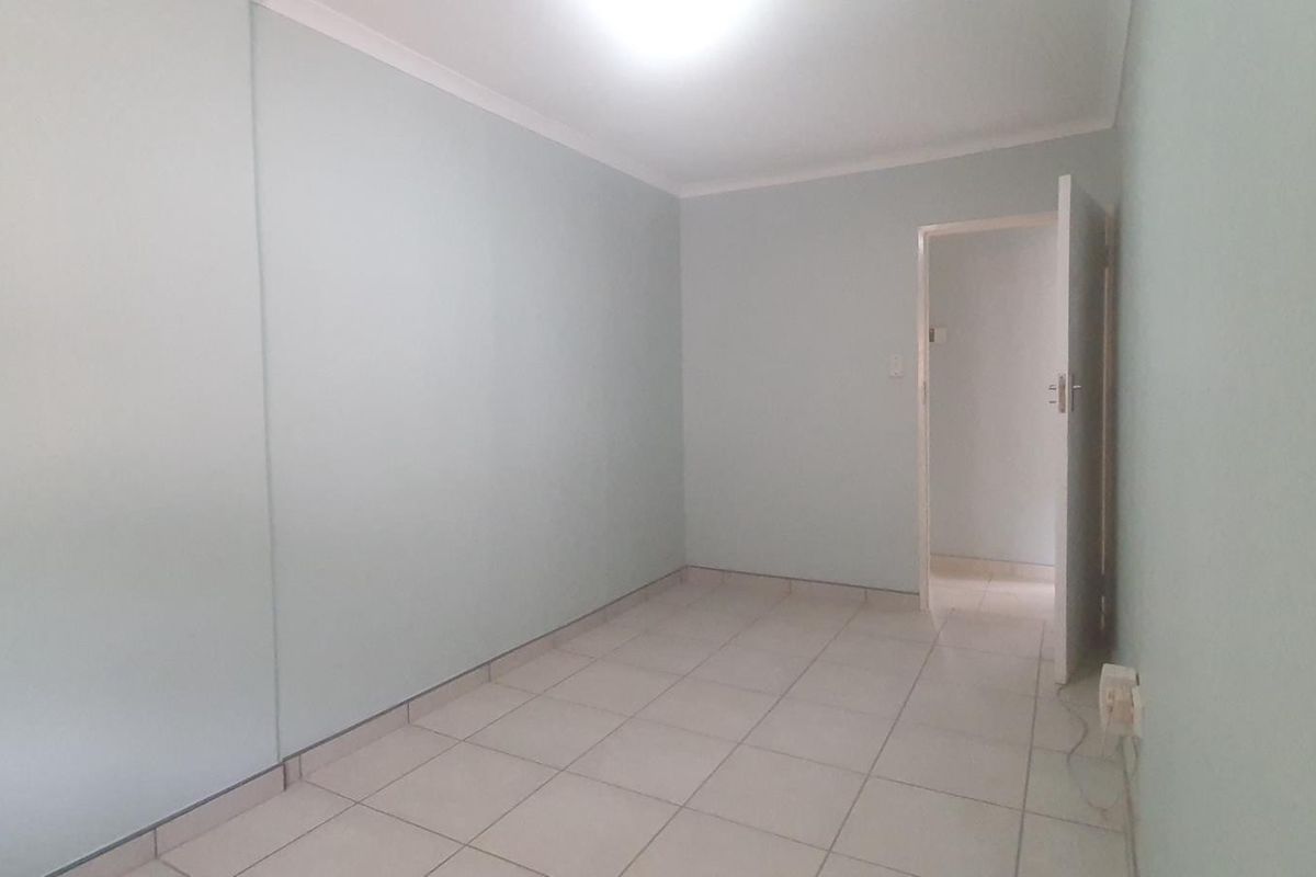 A clean, empty bedroom featuring neutral tiled flooring, built-in wardrobe storage, and simple cornice detailing, ready for personalization.