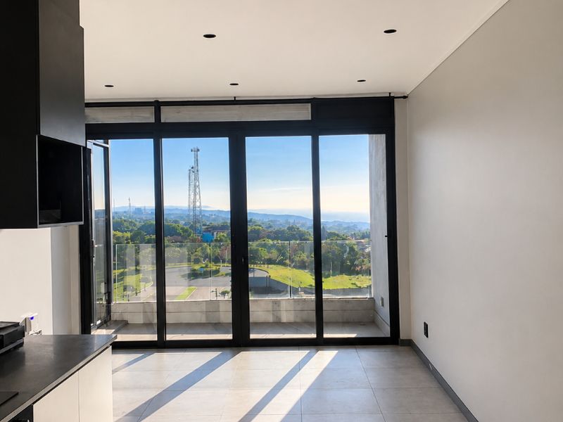 Modern open-plan living area featuring sleek kitchen cabinetry, tiled flooring, and large glass sliding doors opening to a balcony with scenic views.