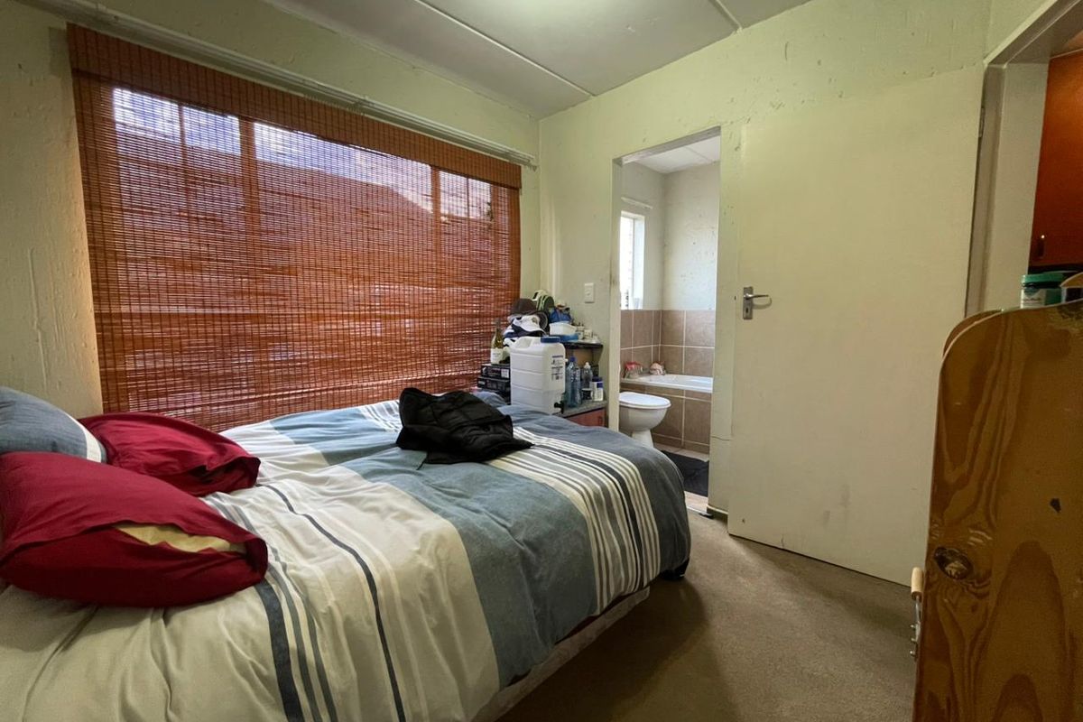 A bedroom featuring carpeted flooring and a window with a bamboo blind, with an adjoining en-suite bathroom visible through the doorway.