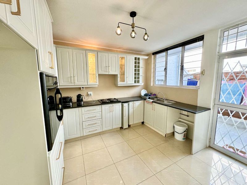 A well-maintained kitchen featuring white cabinetry, granite countertops, built-in oven, hob, and tiled flooring, with direct access to an outdoor area.