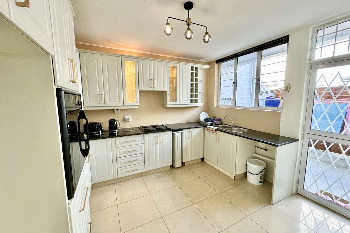 A well-maintained kitchen featuring white cabinetry, granite countertops, built-in oven, hob, and tiled flooring, with direct access to an outdoor area.